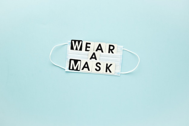 A medical mask and a text message wear a mask on a light blue background Poster banner virus prote