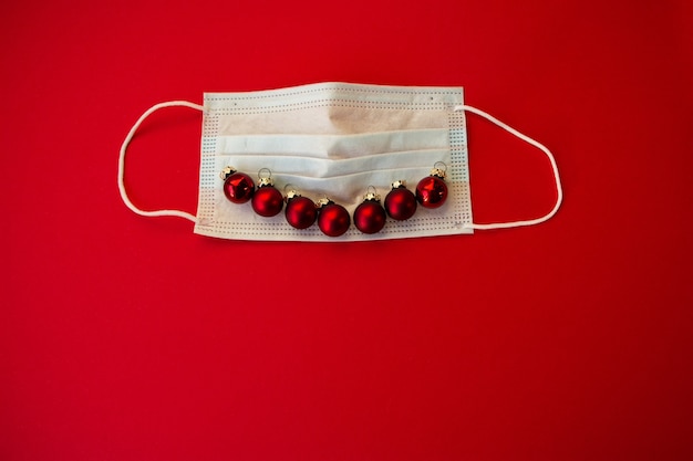 Medical mask with the smiley face of their red Christmas balls on a red background