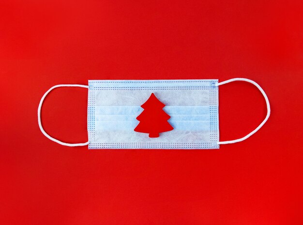 Medical mask and wooden christmas tree on a red surface