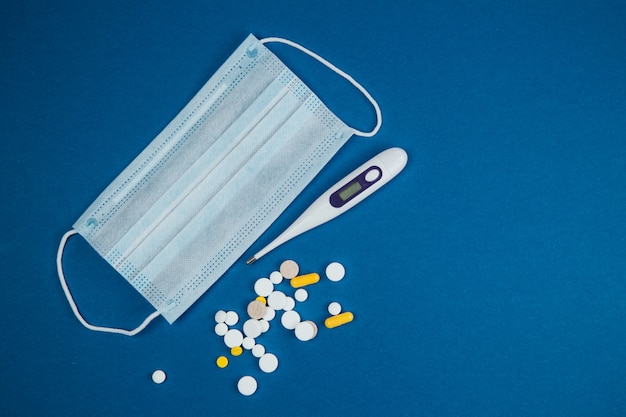 Medical masks and pills, thermometer on a blue background.