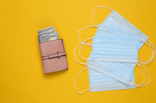 Medical masks and wallet with money on yellow background