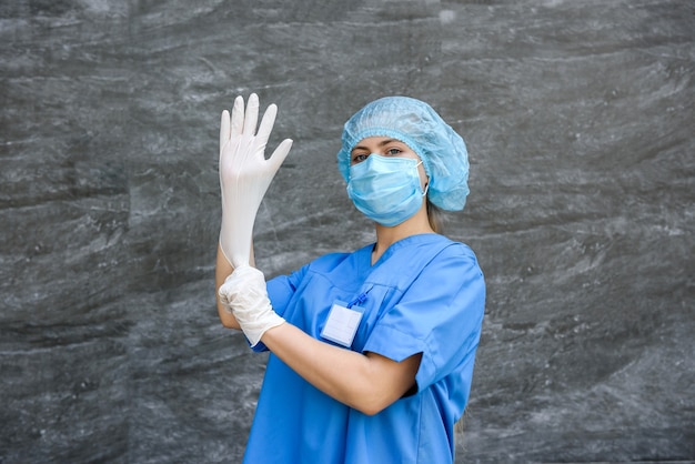 카메라에 포즈를 취하는 potective 균일 한 의료 간호사. 그녀는 파란색 마스크, 모자 및 셔츠를 입고