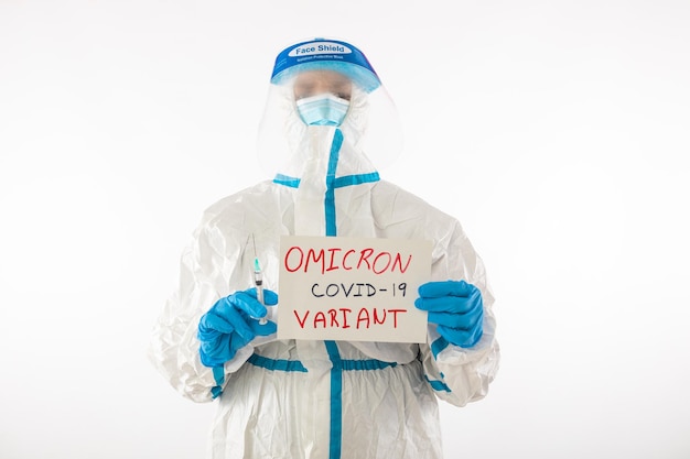 Medical nurse in PPE and latex gloves holding a sign that reads: 'OMICRON VARIANT COVID-19' and in the other hand she holds a needle and a vaccination vial. Coronavirus, pandemic and health concept.