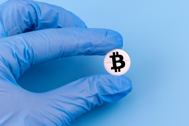 Medical pill with a bitcoin sign in a hand in a medical glove on a blue background Bitcoin technology concept in medicine