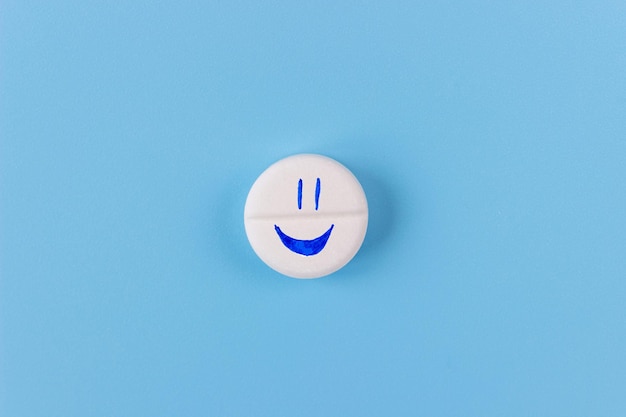 Medical pill with a cheerful face on a blue background. Treatment, medicine, drugs, pills, vitamins, supplements concept.