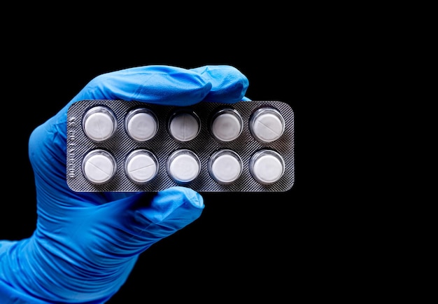 Medical pills in blister on isolated black background with reflection in hand