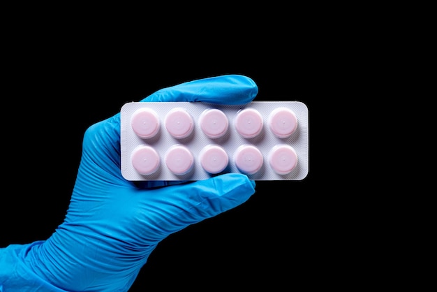 Medical pills in blister on isolated black background with reflection in hand