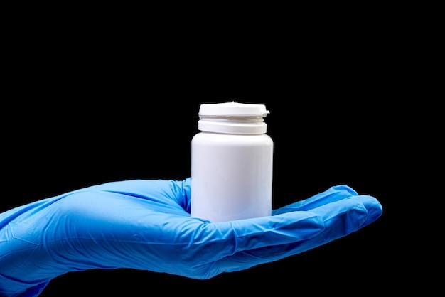 Medical pills in white jar on an isolated black background with reflection in hand