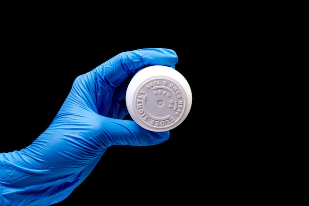 Medical pills in white jar on an isolated black background with reflection in hand