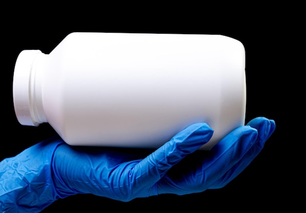 Medical pills in white jar on an isolated black background with reflection in hand