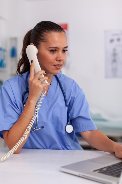 Medical practitioner having a conversation with patient on phone from hospital office and checking a...