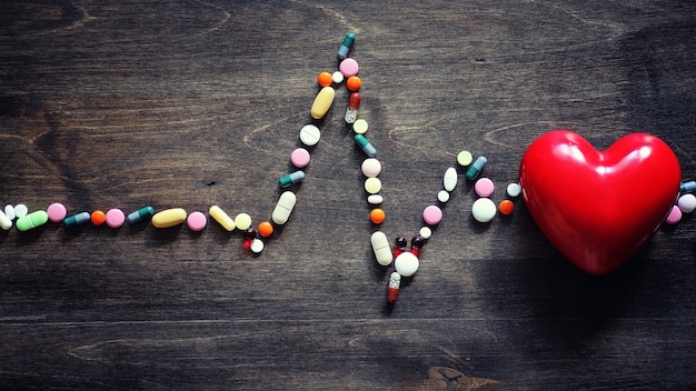 Medical preparations for the treatment of heart diseases. The concept of heart health dependence on tablets. Pills and stethoscope on wooden background.