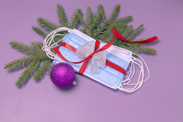 Medical protective face masks tied with a red gift ribbon fir branches and a Christmas ball