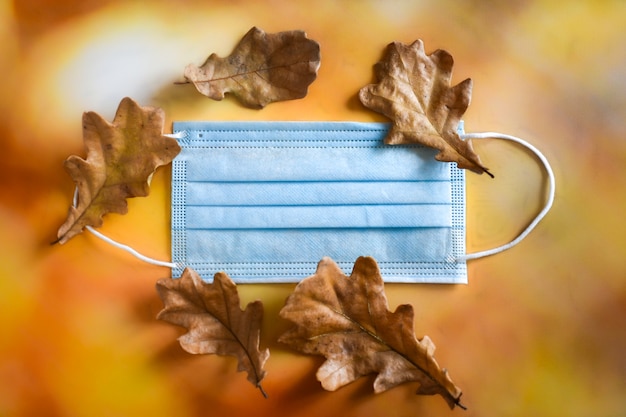 Medical protective mask and dry oak leaves lie on bright autumn background. protection from viruses