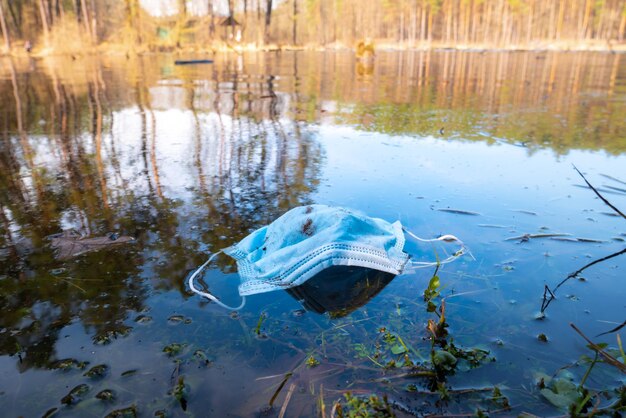 都市湖の水中の医療用保護マスクコロナウイルスの結果COVID19生態系汚染医療ゴミの概念公園内のゴミとゴミ