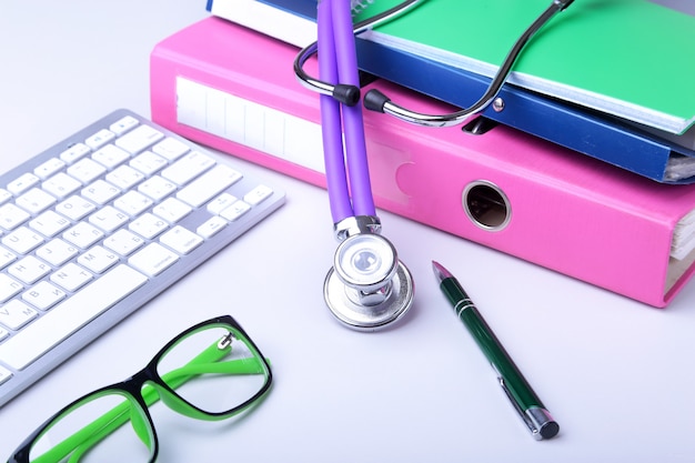 Photo medical record  with stethoscope over pile of folders. keyboard, glasses, pen, rx prescription. selective focus