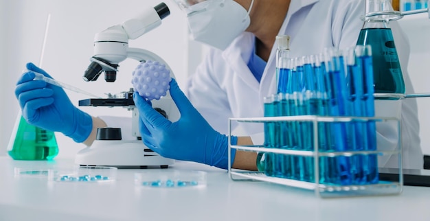 Medical or scientific researcher researching and experimenting multicolored solution vial and microscope in the laboratory or in the laboratory by wearing blue gloves and white clothing completely