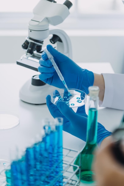 Medical or scientific researcher researching and experimenting Multicolored solution vial and microscope In the laboratory or in the laboratory by wearing blue gloves and white clothing completely