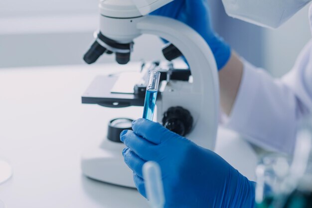 Medical or scientific researcher researching and experimenting Multicolored solution vial and microscope In the laboratory or in the laboratory by wearing blue gloves and white clothing completely