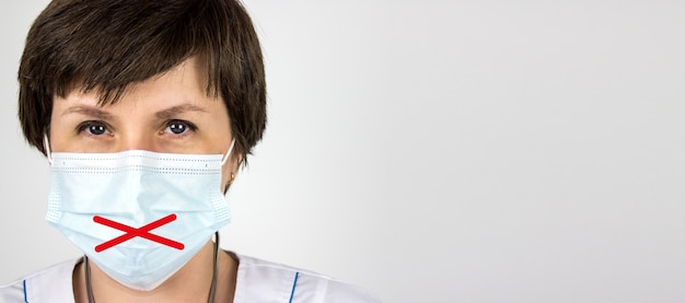 Medical secrecy and nondisclosure of diagnosis concept. Woman doctor in mask with taped lips, white uniform on white background. Medical secrecy concept.