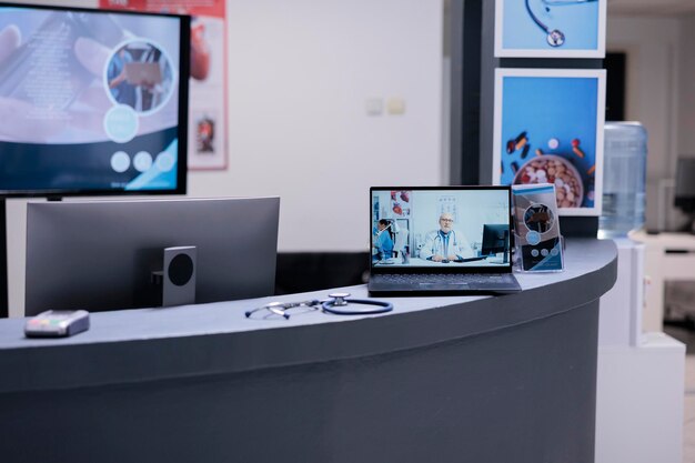 Medical specialist giving consultation via video call on laptop\
at modern sanatorium lobby desk. general practitioner attending\
patients in reception area of hospital through computer.