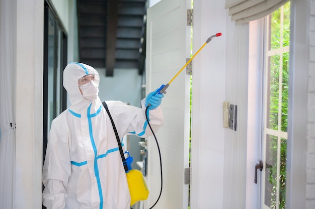 A medical staff in PPE suit is using disinfectant spray in living room, Covid-19 protection , disinfection concept .