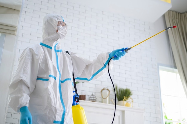 Uno staff medico in tuta dpi sta usando spray disinfettante in soggiorno, protezione covid-19, concetto di disinfezione.