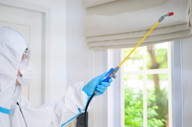 A medical staff in PPE suit is using disinfectant spray in living room, Covid-19 protection , disinfection concept .