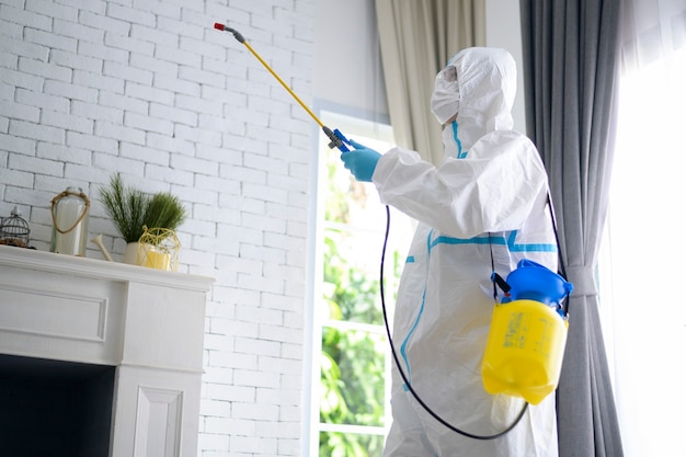 Uno staff medico in tuta dpi sta usando spray disinfettante in soggiorno, protezione covid-19, concetto di disinfezione.