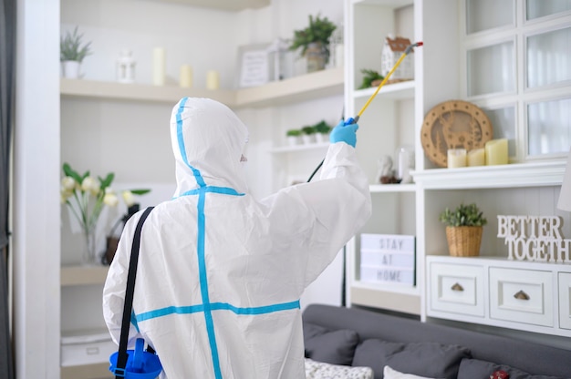 A medical staff in PPE suit is using disinfectant spray in living room