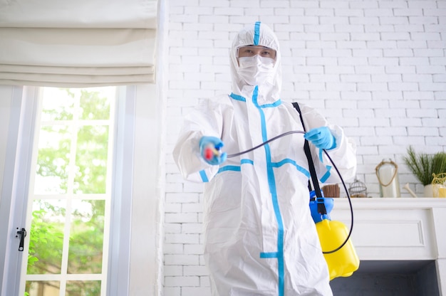 a medical staff in ppe suit is using disinfectant spray in living room