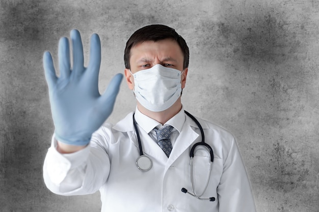 Medical staff preventive gear against coronavirus. Male doctor in face mask showing stop sign with his hand.