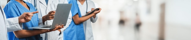 의사, 간호사 및 전문가가 함께 작업하는 의료진 팀은 노트북과 태블릿을 사용하여 병원 복도 배경에서 흐릿하게 작업합니다.