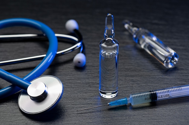 Medical stethoscope and ampoules with a vaccine or medicine on grey table