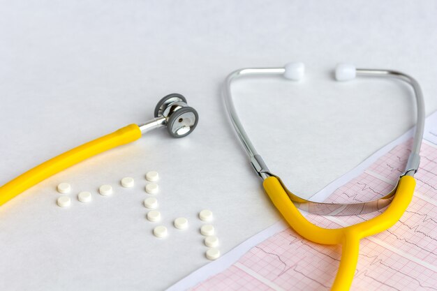 Medical stethoscope on cardiogram chart with a pills, tablets and capsules, close up.