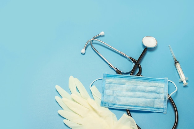 Medical stethoscope, latex gloves, syringe and protective mask on a blue. Concept medicine, nurse, hospital, safety, epidemic.