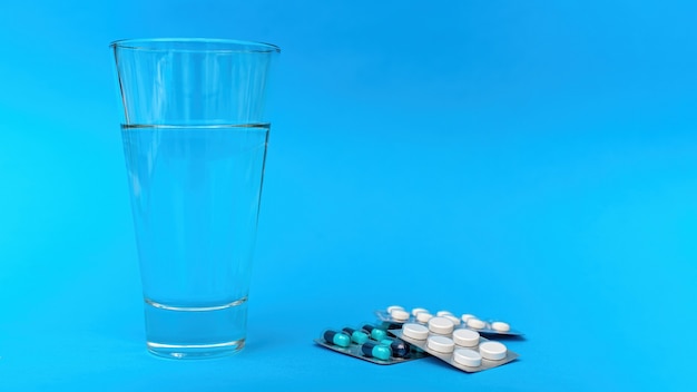 Medical supplies and items composition on blue background. Stack of pill packs with a cup of water