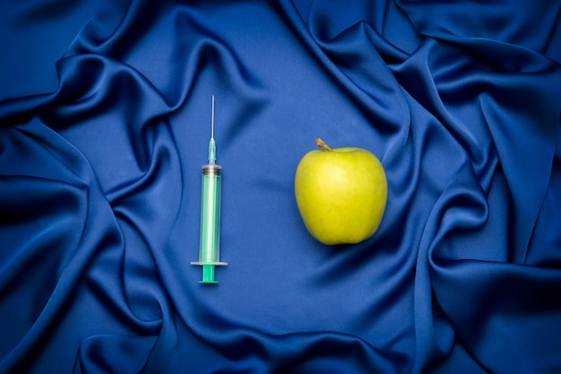 Medical syringe and apple on a blue