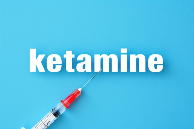 케타민이라는 단어의 배경에 있는 의료 주사기 텍스트 미니멀리즘 평면 층