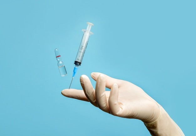 A medical syringe balances on the tip of a human finger.