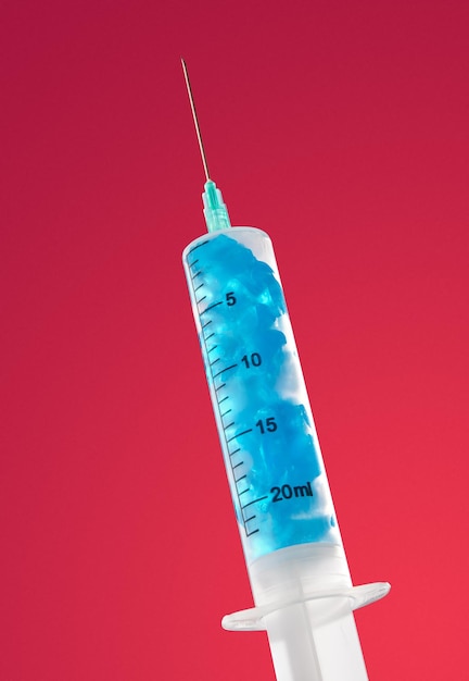 Medical syringe filled with blue contents on red background Aesthetic concept of health