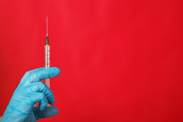 medical syringe for injection in the hand of a doctor in a glove on a red background