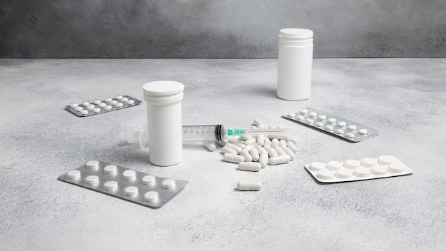 Medical syringe, medicine pills, capsules, vials, on grey concrete