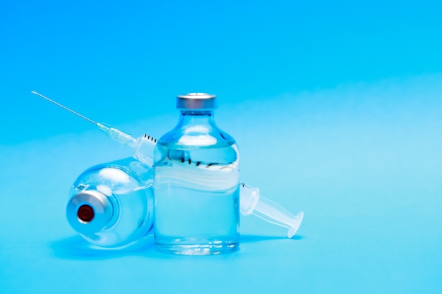 Medical syringe with needle incline on sealed glass capsule of transparent liquid as medicine or vaccine dose for doctor to cure disease or activate immunity of patient against pathogen.