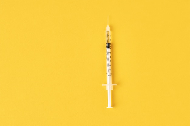 Medical syringe on yellow, top view with copy space. Vaccination and virus protection concept