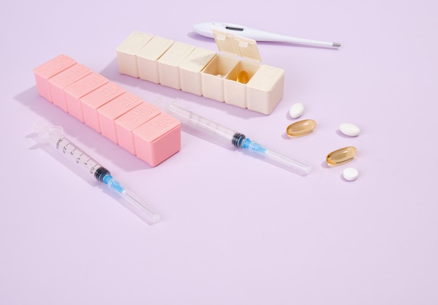 Medical syringes for injections pills and capsules to treat illnesses a thermometer to measure temperature and pill boxes on a purple background