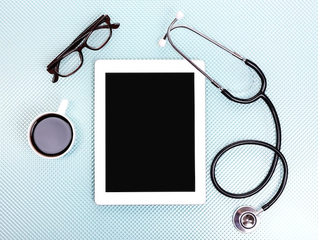 Medical tablet stethoscope glasses and coffee cup on blue background