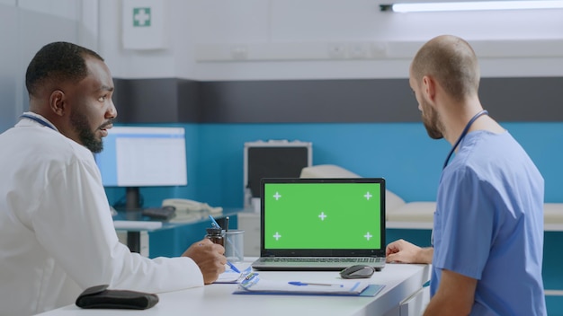 Medical team discussing disease symptoms analyzing diagnostic report working at healthcare treatment in hospital office. Mock up green screen chroma key laptop computer with isolated display