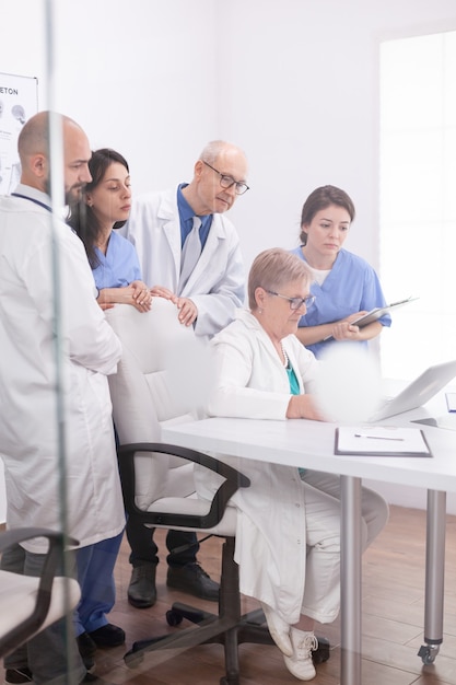 Medical team having a discussion about patient diagnosis looking at laptop screen in conference room. Clinic expert therapist talking with colleagues about disease, medicine professional.