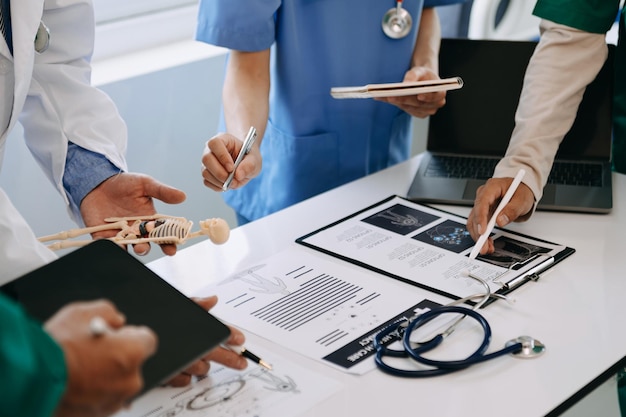 Medical team having a meeting with doctors in white lab coats and surgical scrubs seated at a desk discussing a patients working online using computers in the medical industryxA